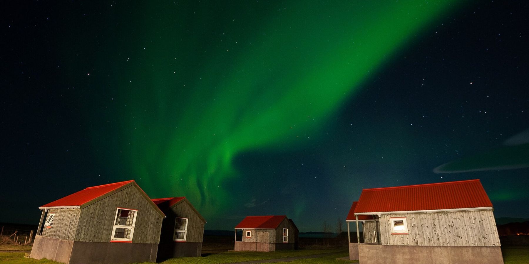 Aurora boreale verde sopra alcune case dal tetto rosso in Islanda